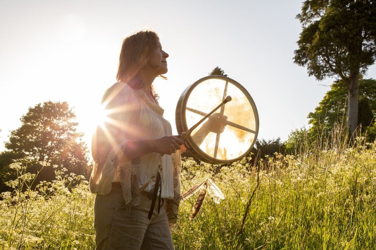 A woman stands in a field banging a drum during a forest bathing experience