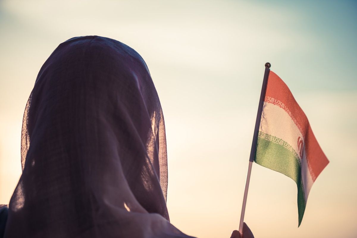 A woman wearing a headscarf waves an Iranian flag