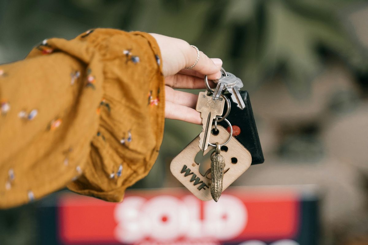 A woman with a yellow sleeve holds a bunch of keys in front of a 'sold' sign