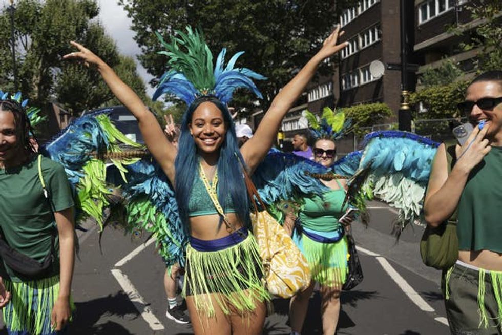 A woman with blue hair and a feathered headdress waves her hands in the air