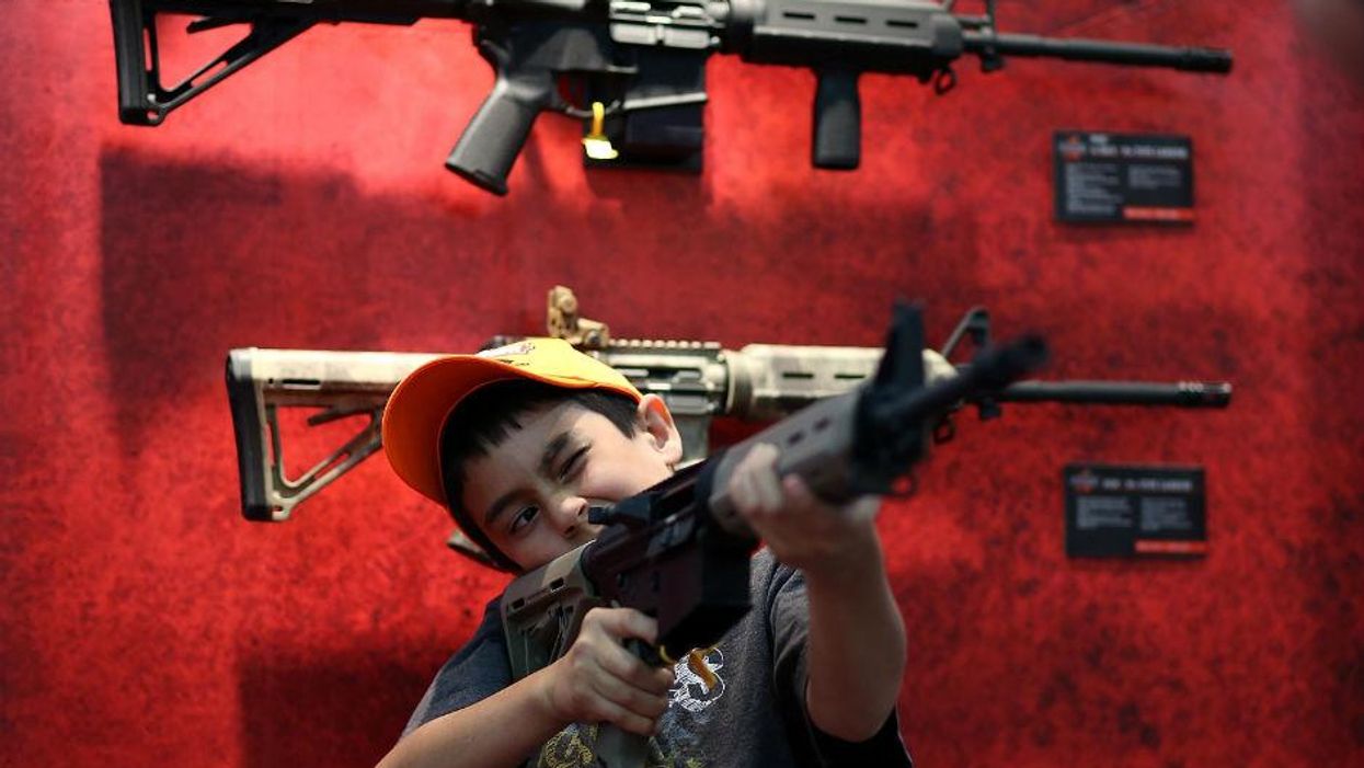 A young attendee inspects an assault rifle during the 2013 NRA Annual Meeting
