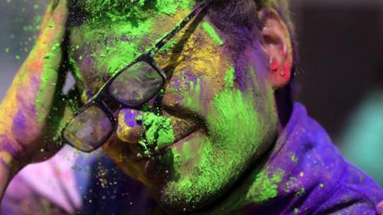 A young man is smeared in powdered colors by his friend as they take part in Holi festival celebrations at Durgiana Temple