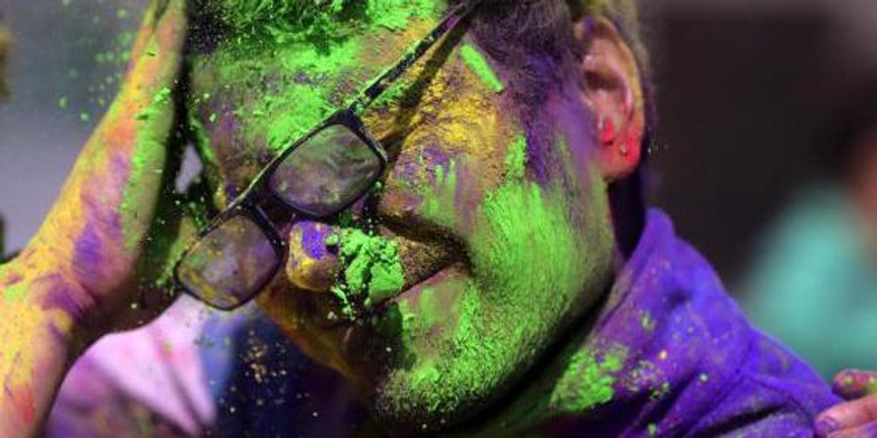 A young man is smeared in powdered colors by his friend as they take part in Holi festival celebrations at Durgiana Temple