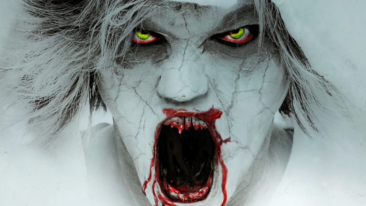 A zombie with a white, chalky face and cracked skin, with bloody, jagged teeth, yellow eyes and matted hair, screams at the camera.