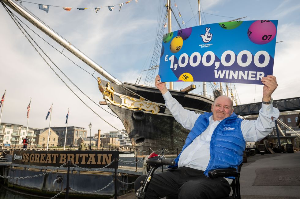 Alan Wilcock holding a sign above his head reading '\u00a31,000,000 winner' in front of the SS Great Britain