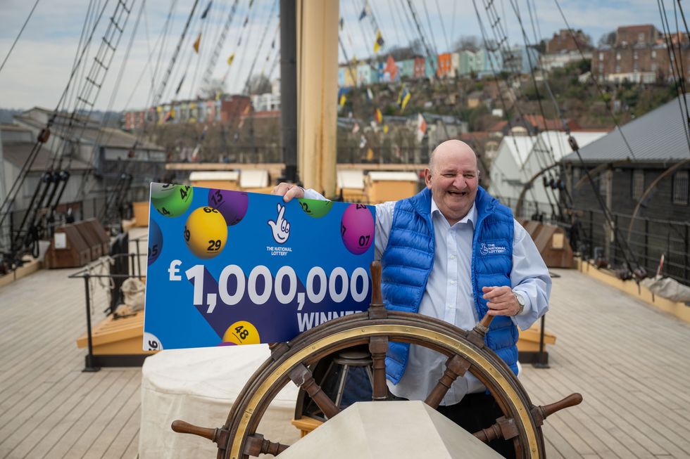 Alan Wilcock smiling while holding the wheel of a ship, and a poster reading '\u00a31,000,000 winner'