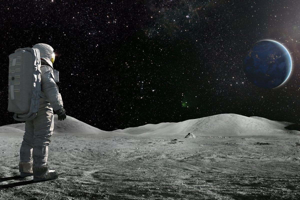 An astronaut stands on the surface of the Moon and gazes over at planet Earth