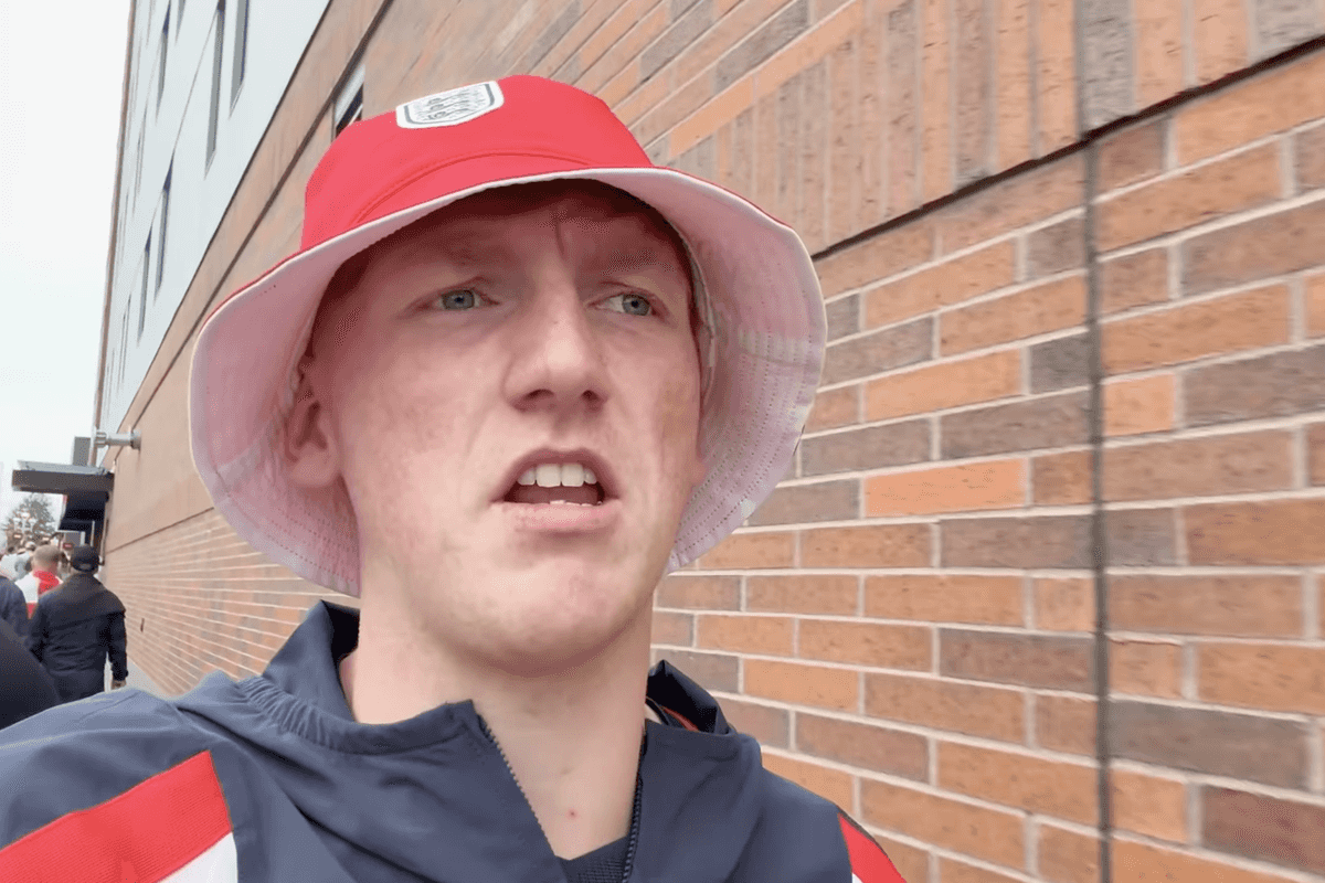 AngryGinge, a white man with ginger hair and a red bucket hat, talks to the camera as he walks out of a football stadium.