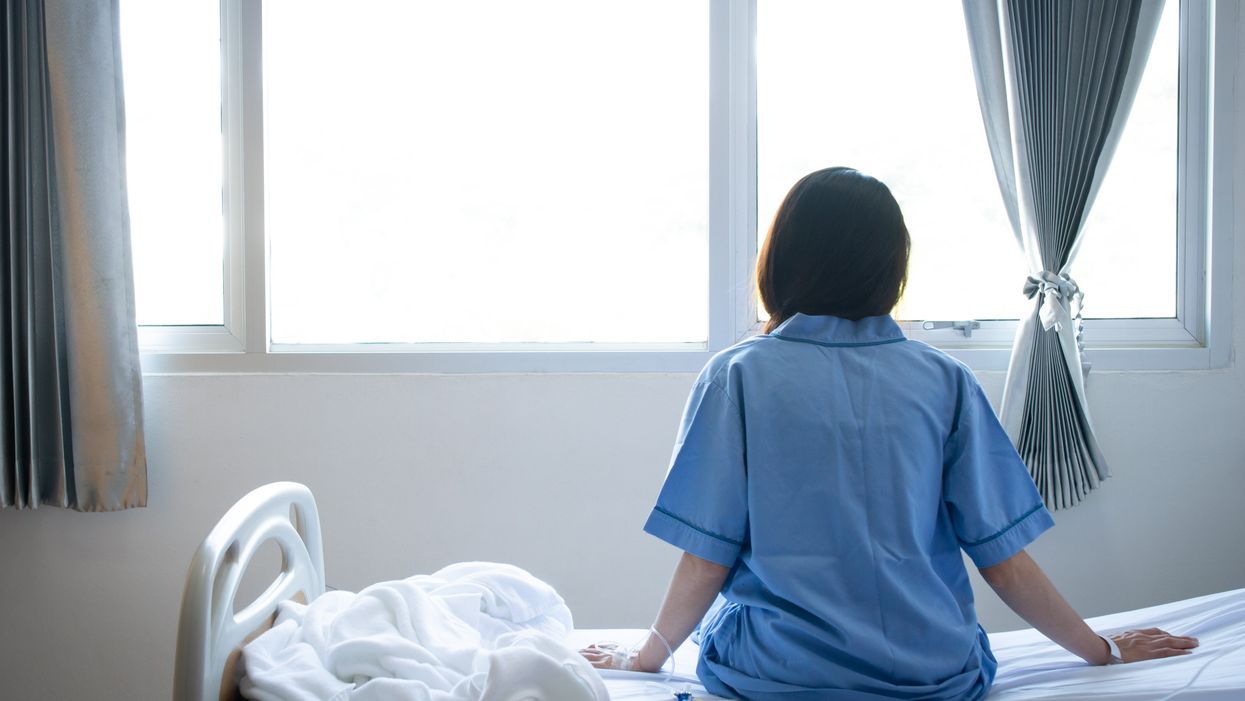 <p>Back view of patient woman sitting on bed in hospital ward. (Stock Image). </p>