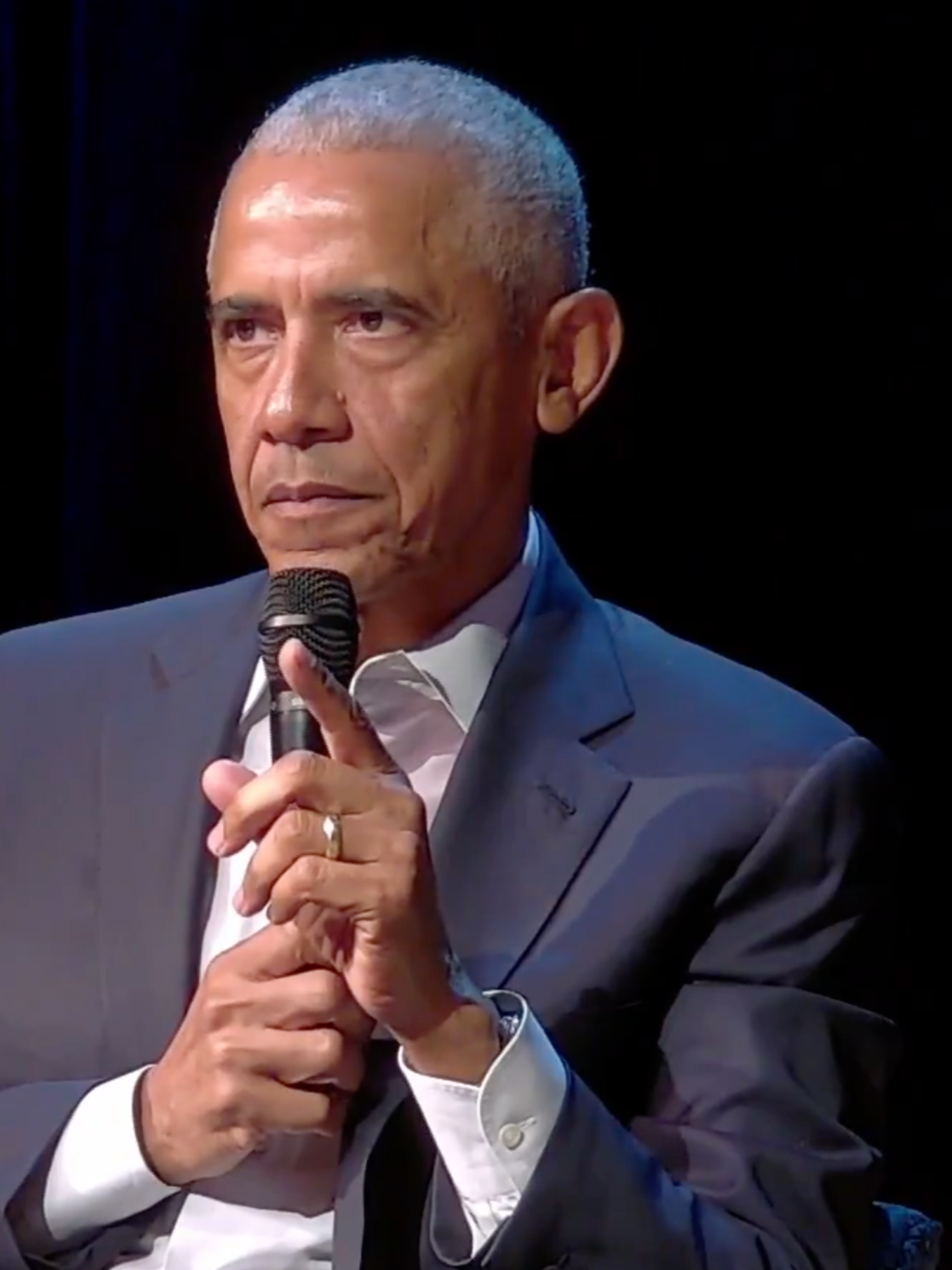 Barack Obama looks out at an audience with a stern expression on his face, holding a microphone.