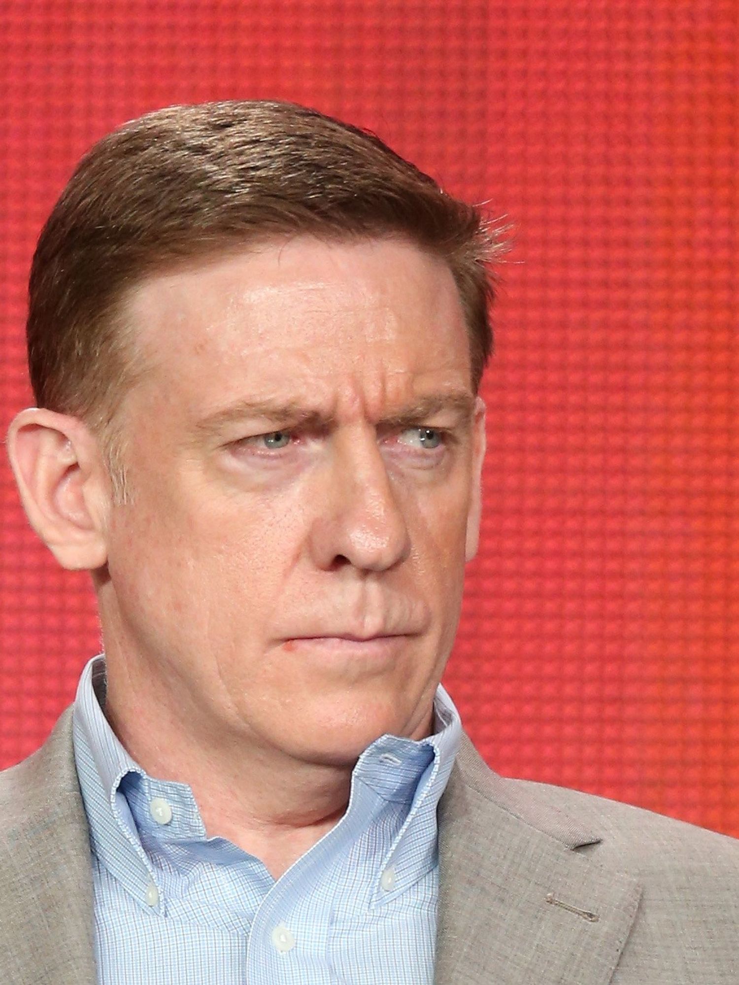 Bill Owens, a white man with short brown hair, sitting on stage and giving a stern look to someone on his left.