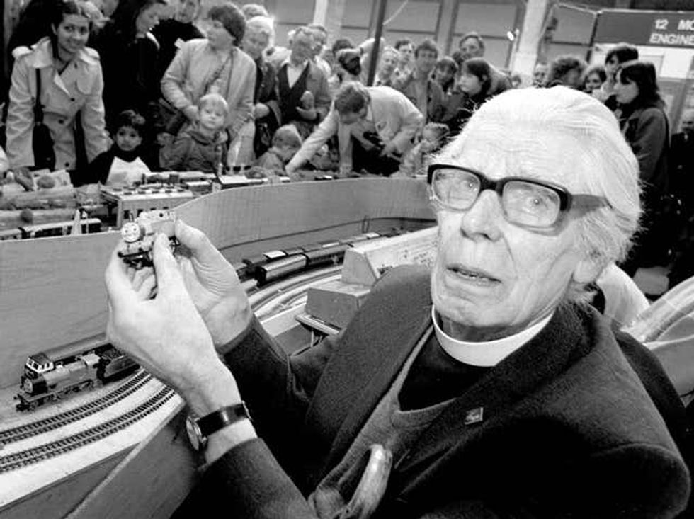 Black and whte image of Rev Wilbert Awdry next to a model railway and holding a mini Thoas engine