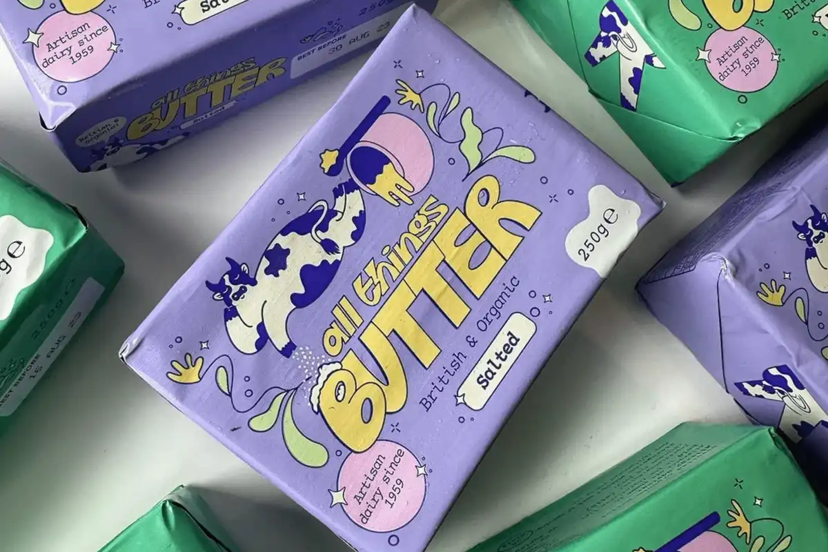 Blocks of All Things Butter butter sits in purple and green packaging on a flat surface