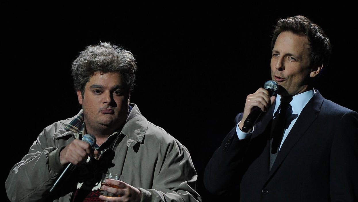 Bobby Moynihan in a grey jacket, holding a glass of whisky as ‘Drunk Uncle’. To the left of him is Seth Meyers in a black suit.