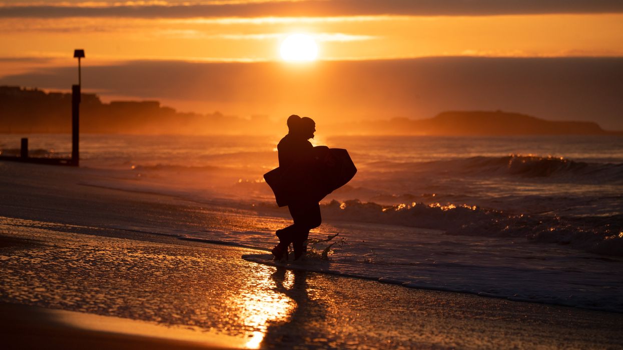 Bodyboarders make their way into the sea as the sun rises over Boscombe beach in Dorset