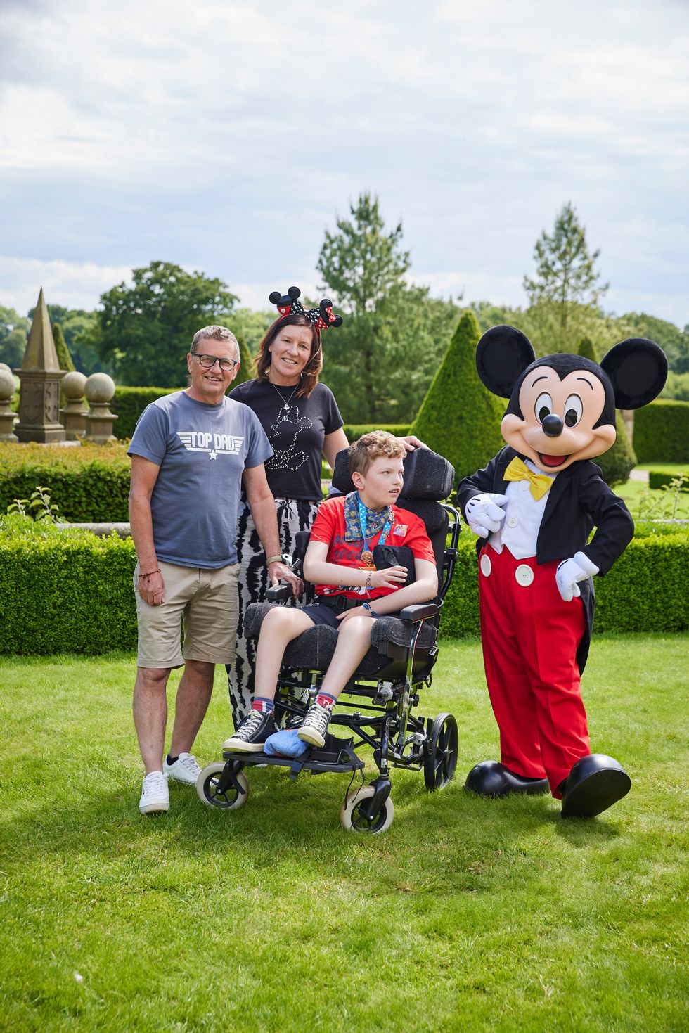 Boy in wheelchair with parents and a man dressed as a mouse