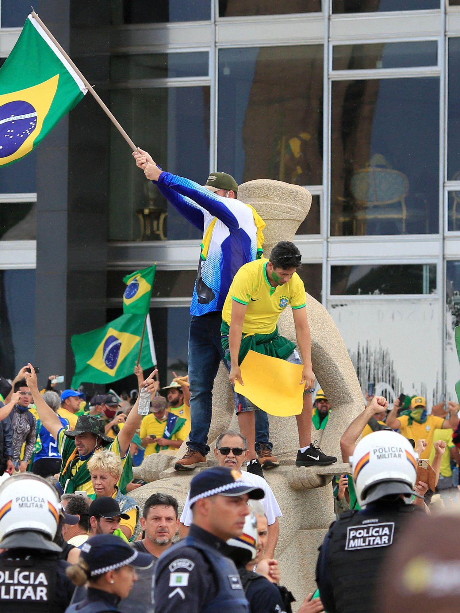 Brazilians in yellow and green shirts waving Brazil flags outside a building while being surrounded by police.