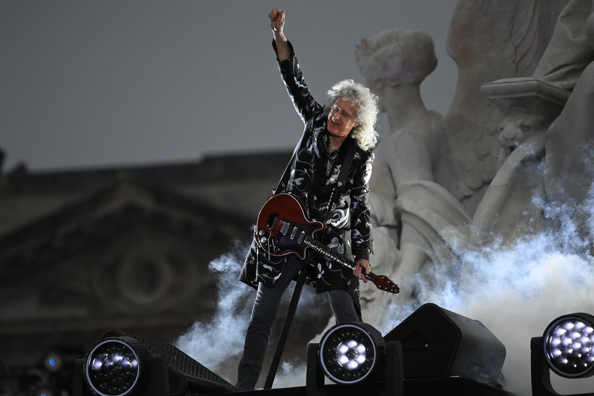 Brian May plays guitar on stage outside Buckingham Palace while wearing a long PVC coat