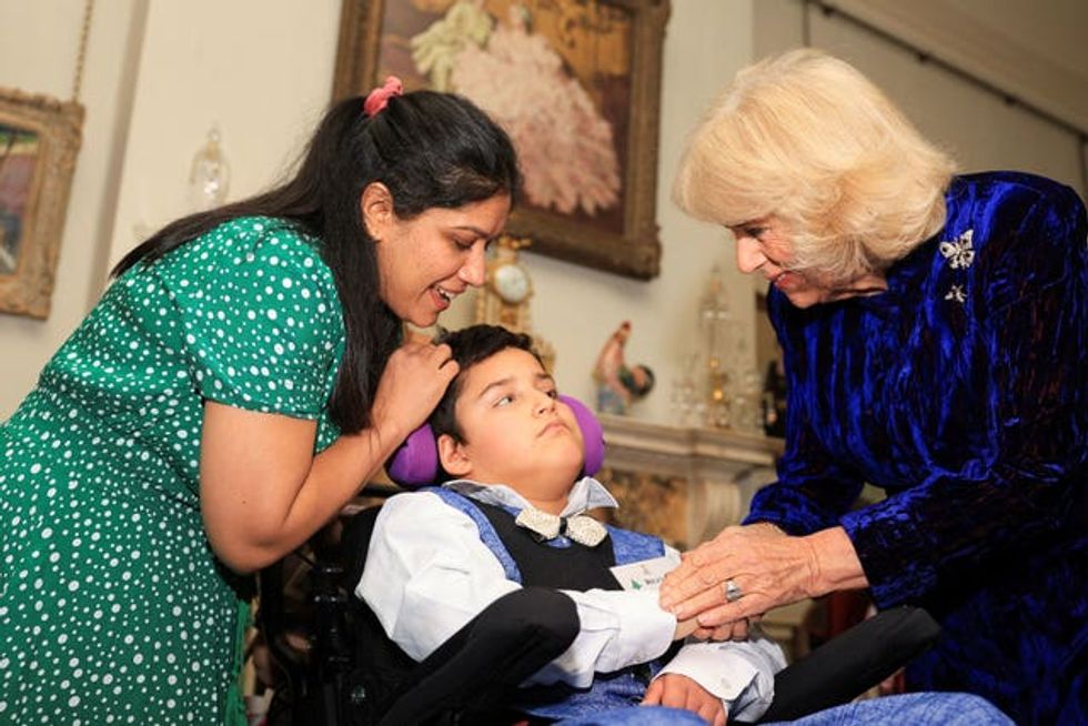 Camilla shaking hands with a child who is wearing a bow tie as his mother watches