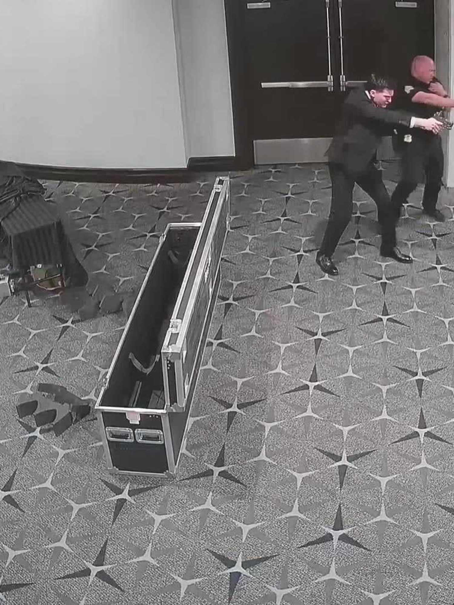 CCTV footage of federal agents pointing their guns at someone off-camera in a hotel lobby.