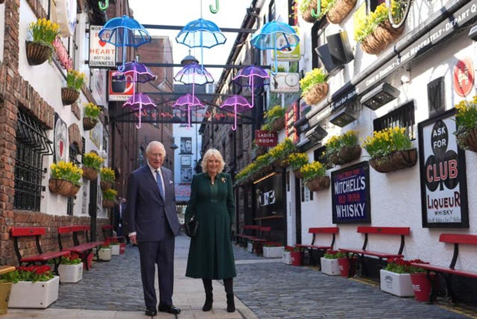 Charles and Camilla standing underneath illuminated umbrellas on Commercial Court in Belfast