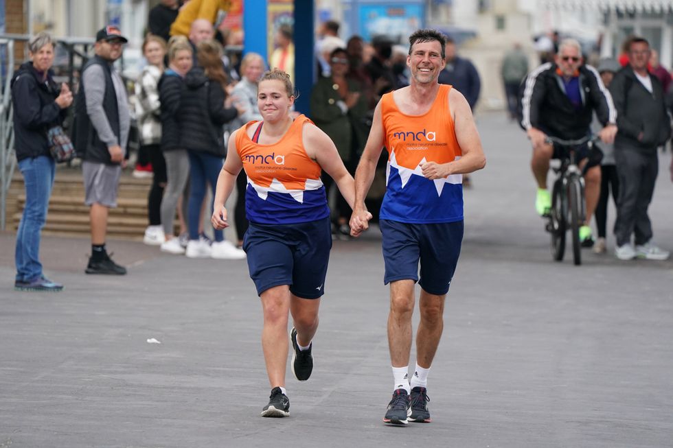 Charlotte Nichols and Stuart Bates hold hands as they run towards the finish line of their marathon at Weymouth Beach (Andrew Matthews/PA)