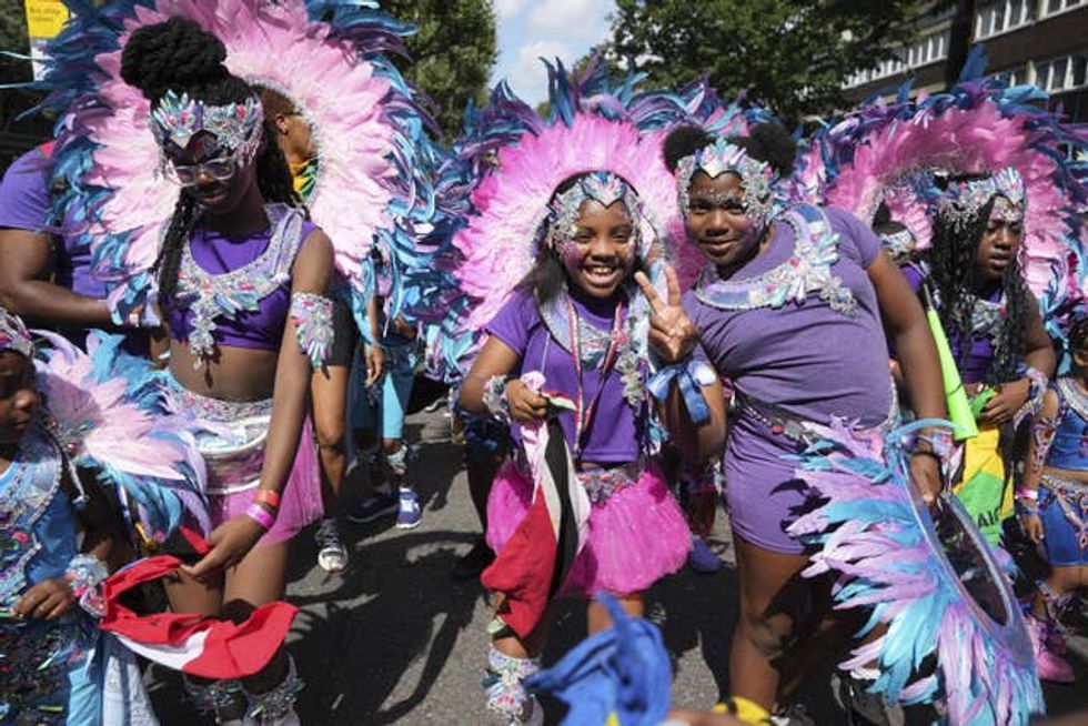 Children in purple with pink features wave at the camera