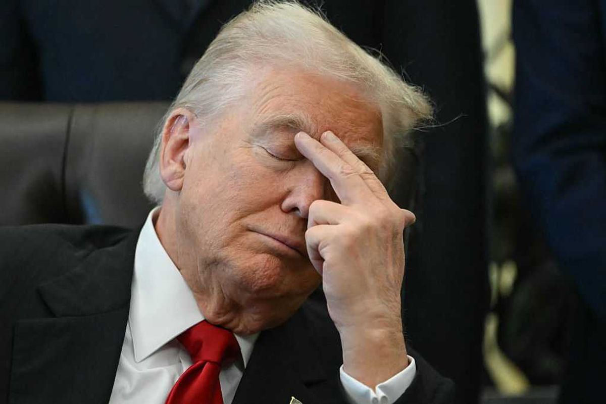 Close-up image of Donald Trump, with his eyes closed, placing his left index finger and middle finger to his right eyebrow as he sits in his chair in the Oval Office.