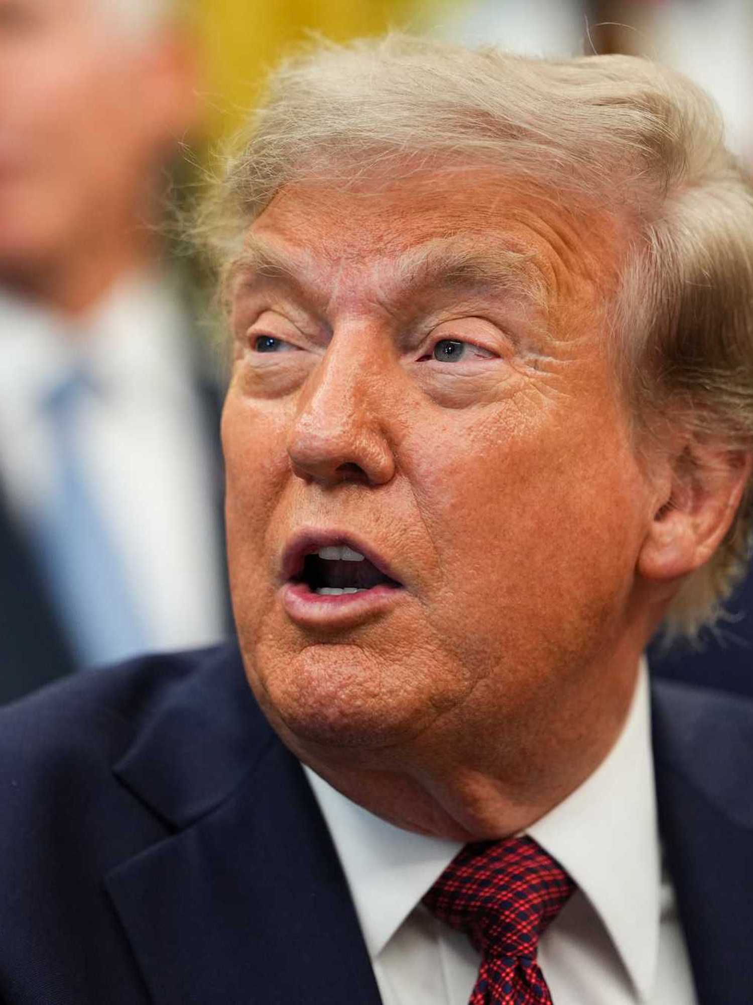 Close-up of Donald Trump looking to his right and speaking to reporters in the Oval Office.