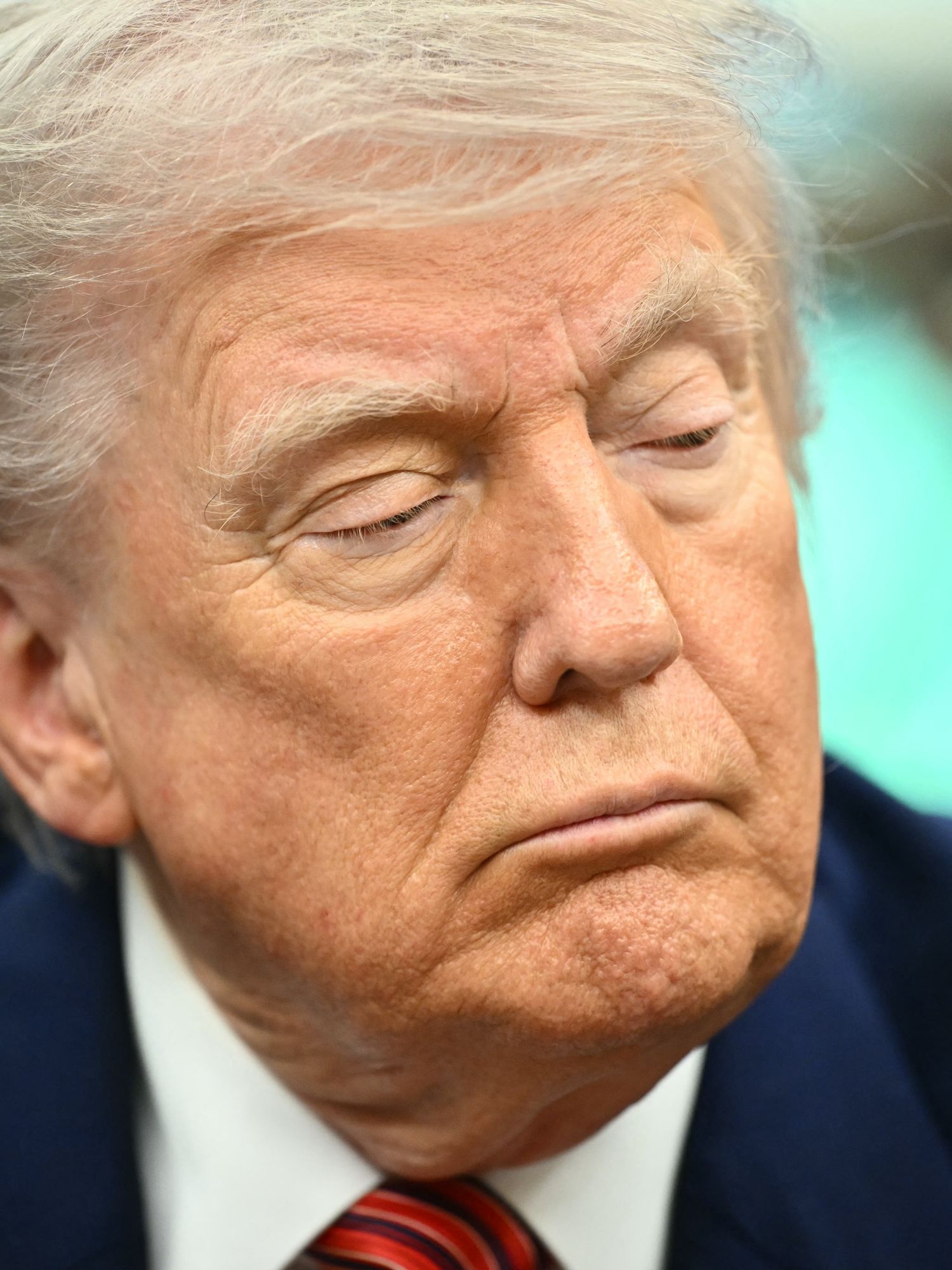 Close up of Donald Trump with a neutral expression on his face, looking out of the corner of his eye at something on his left.