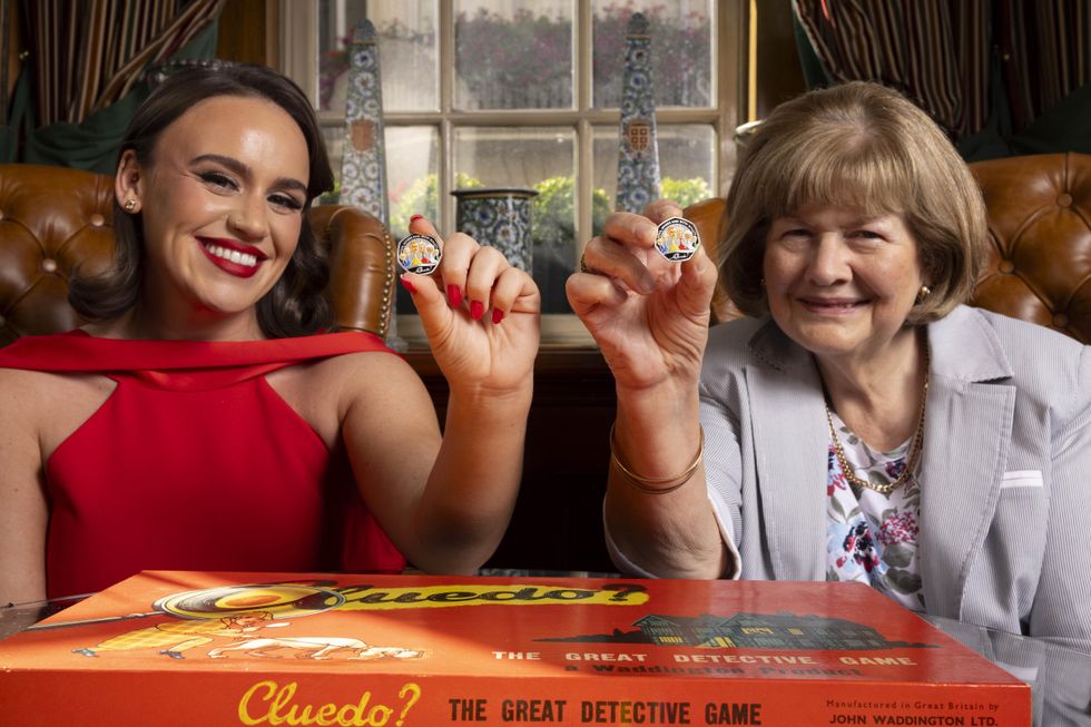 Cluedo coins being held up with a Cluedo game