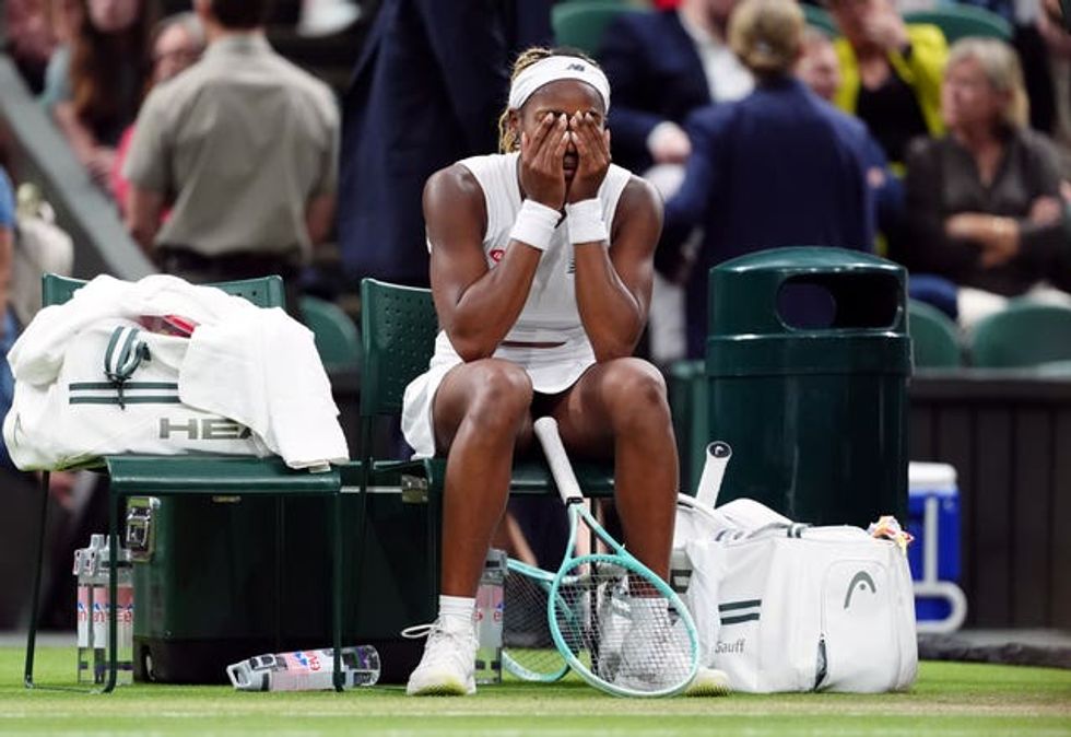 Coco Gauff sitting with her head in her hands by the side of a tennis court