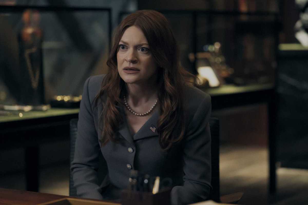 Colby Minifie as Ashley Barrett in The Boys. She's a white woman with wavy brown hair, sitting at a table with a concerned look on her face.