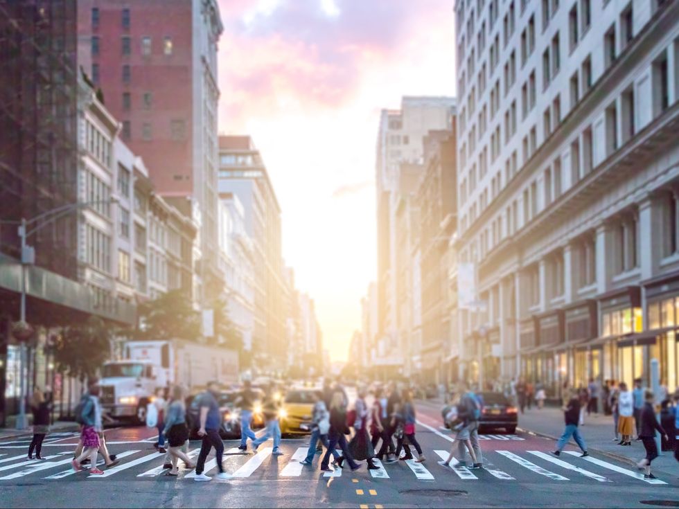 Crowds of diverse people cross the busy intersection on 23rd Street and 5th Avenue in Manhattan with rush hour traffic in the background