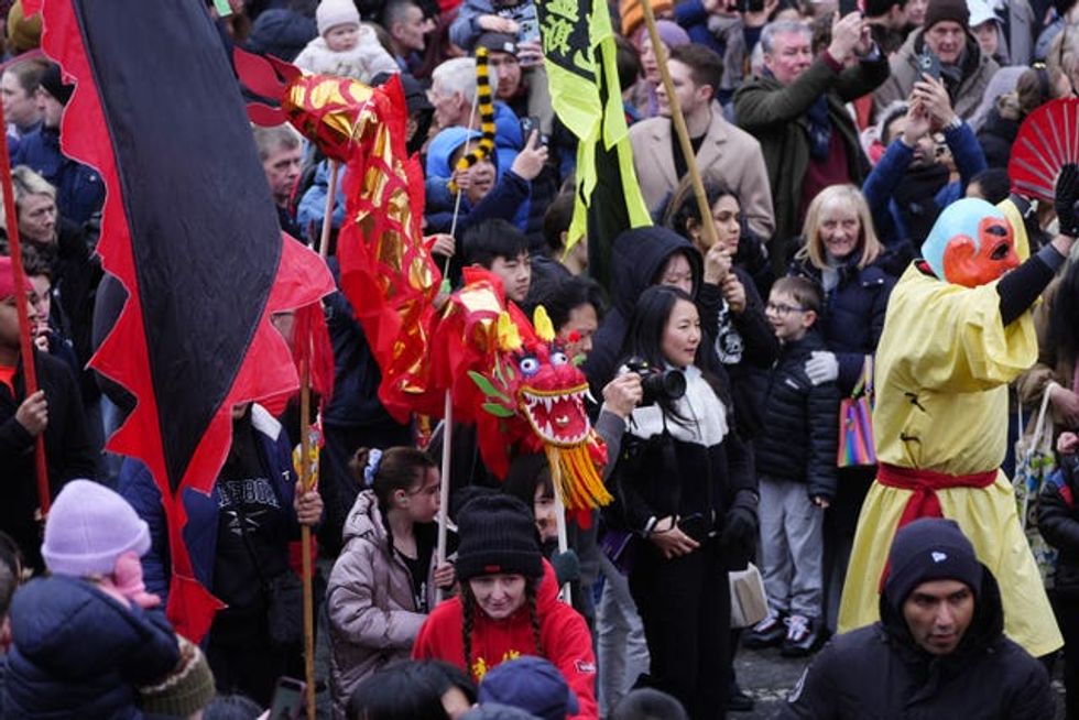 Crowds watch as performers walk past with colourful props