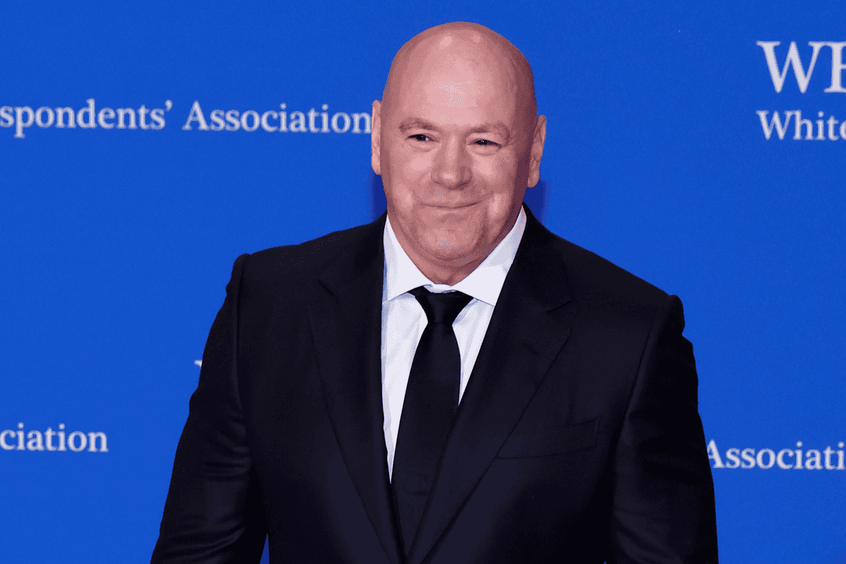 Dana White, a bald white man in a black suit and tie, smiles in front of a blue poster board with the text 'White House Correspondents Association' on it.