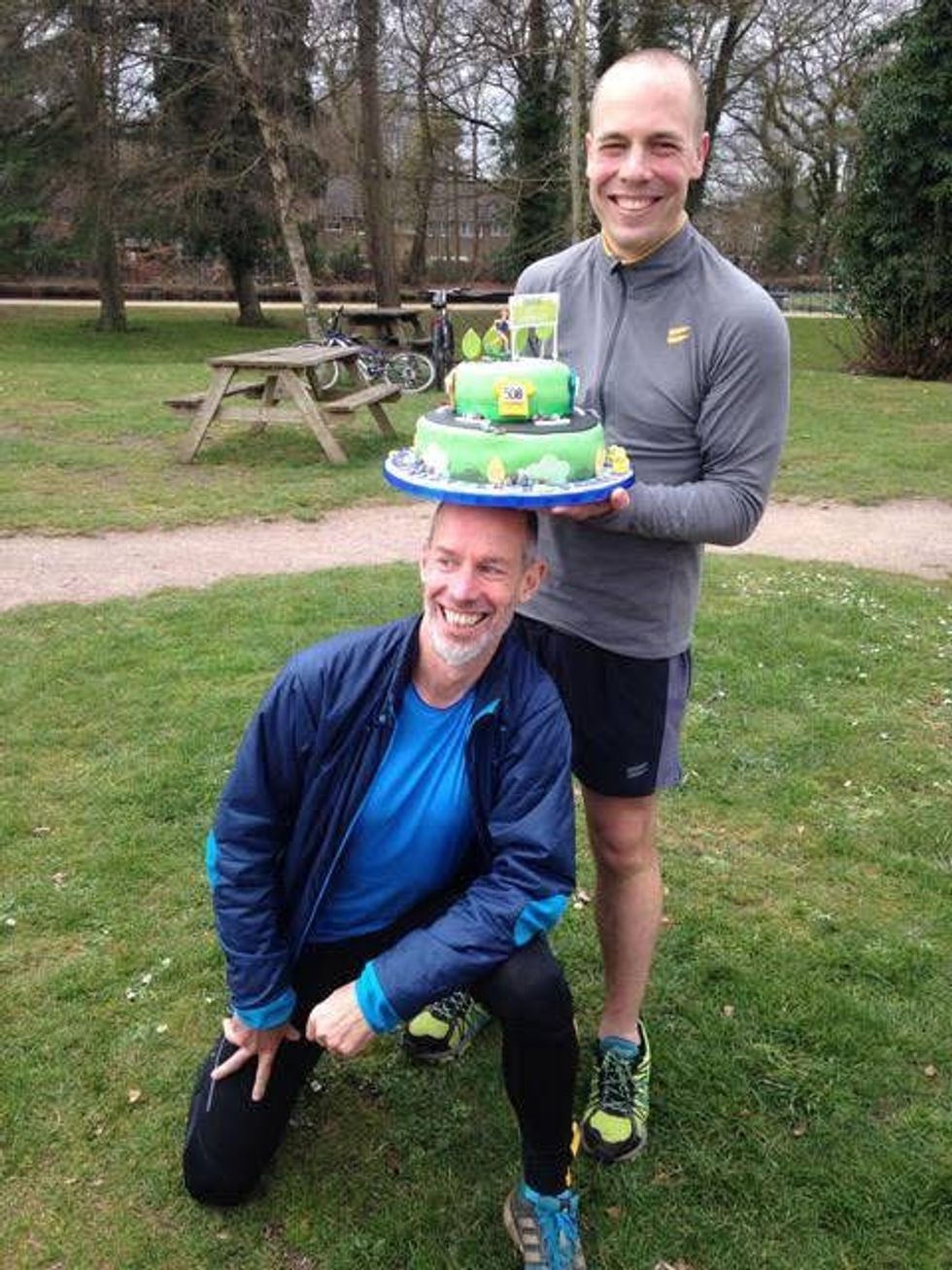 Darren Wood holding a cake celebrating his 500th parkrun with event founder Paul Sinton-Hewitt who is kneeling below the cake