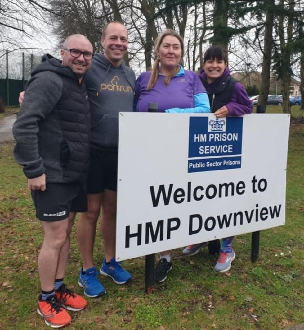 Darren Wood with parkrun volunteers at a sign for HMP Downview in Sutton, Surrey