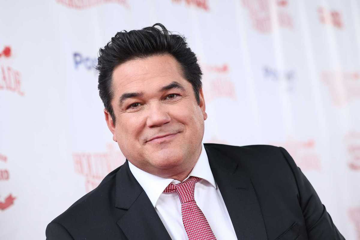 Dean Cain, a white man with short black hair, a black suit and striped red tie.