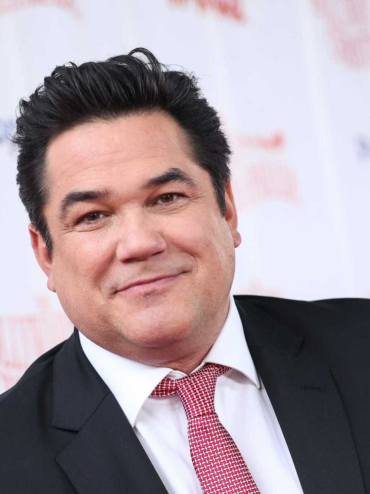 Dean Cain, a white man with short black hair, a black suit and striped red tie.