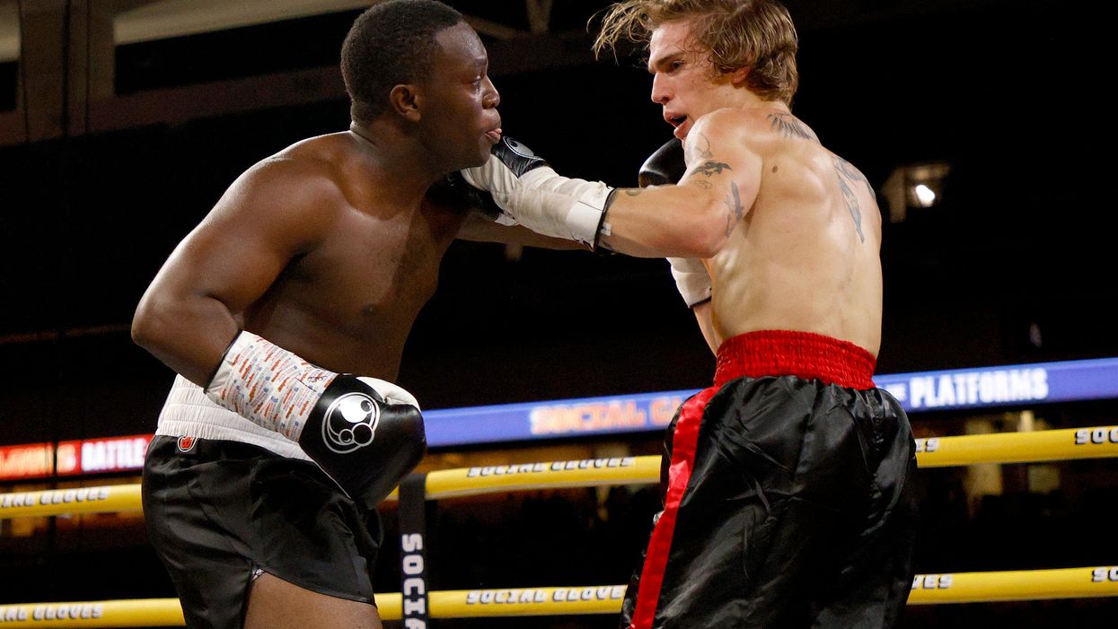 Deji, a Black man, is on the left with black gloves. On the right, Vinnie Hacker, a white man with white gloves, lands a punch under Deji’s chin.