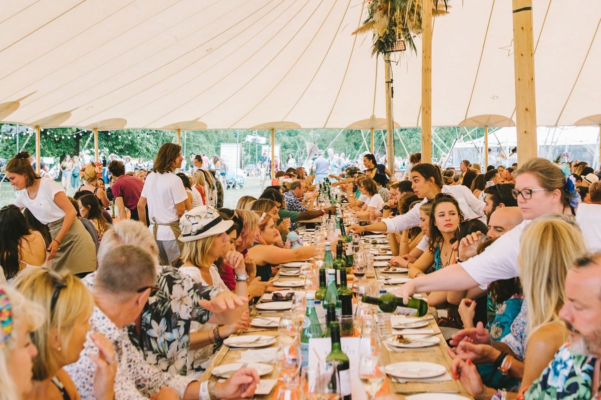 Diners enjoy food and wine sat at a long banquet table