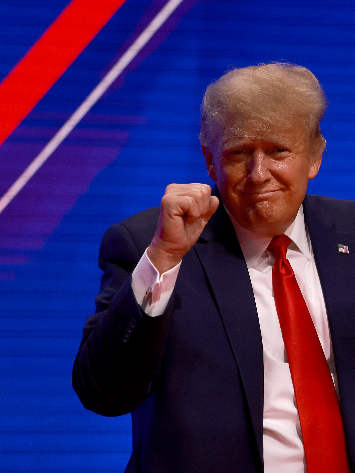 Donald Trump, a white man with bushy blonde hair, a red tie and black suit, dances on stage.