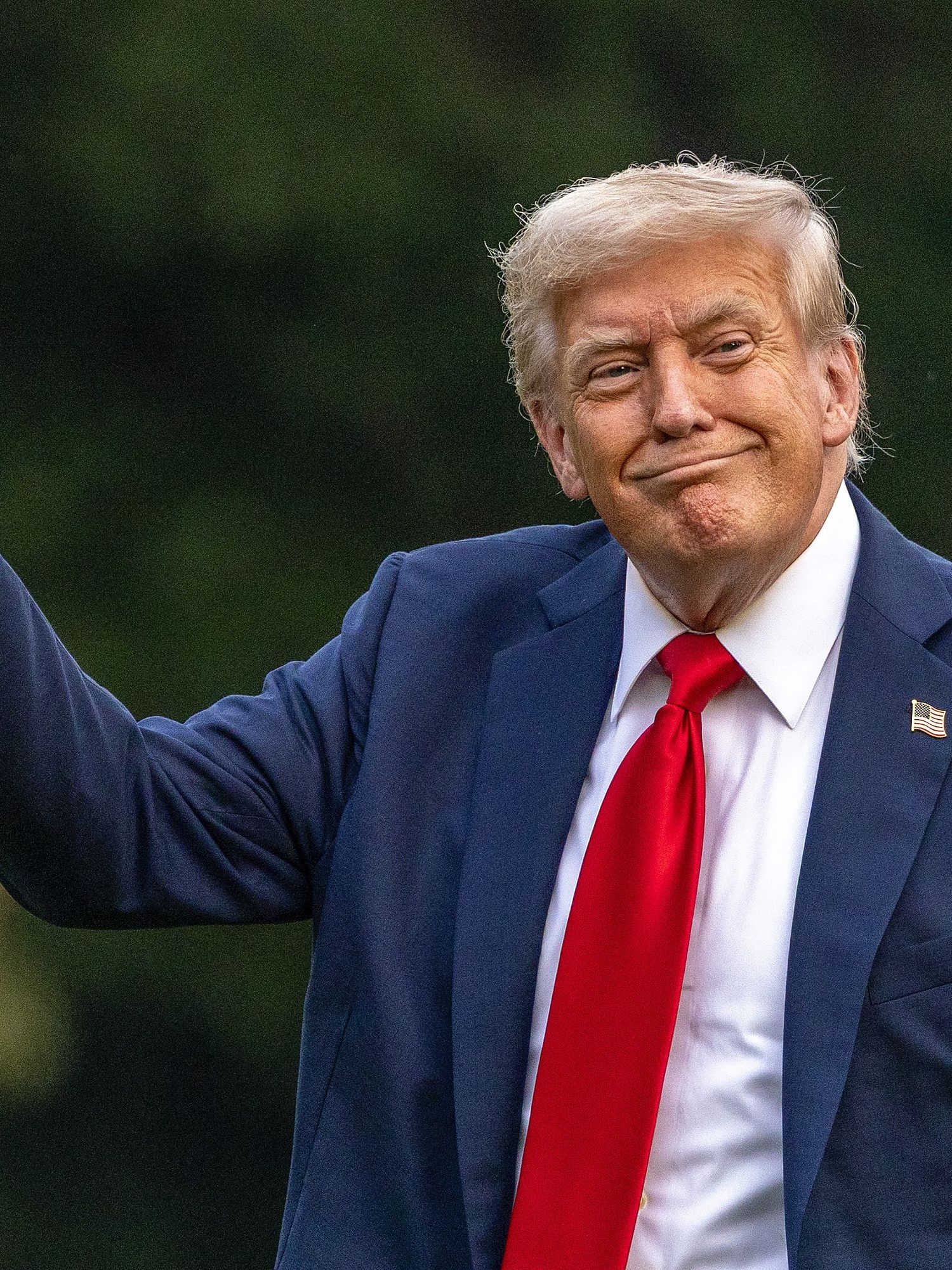 Donald Trump, a white man with short blonde hair, a blue suit and red tie, smiling as he points with his right index finger.