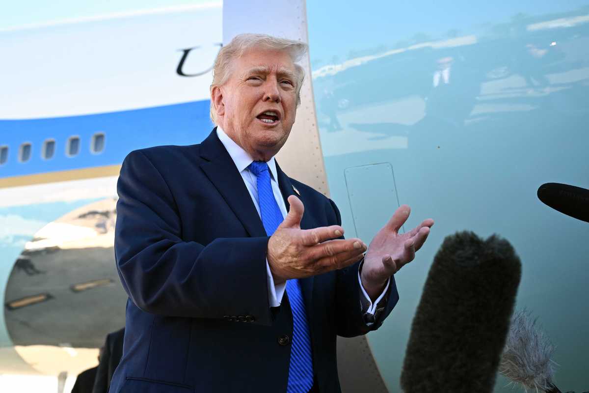 Donald Trump, a white man with short blonde hair and a black suit, talking to reporters next to Air Force One.