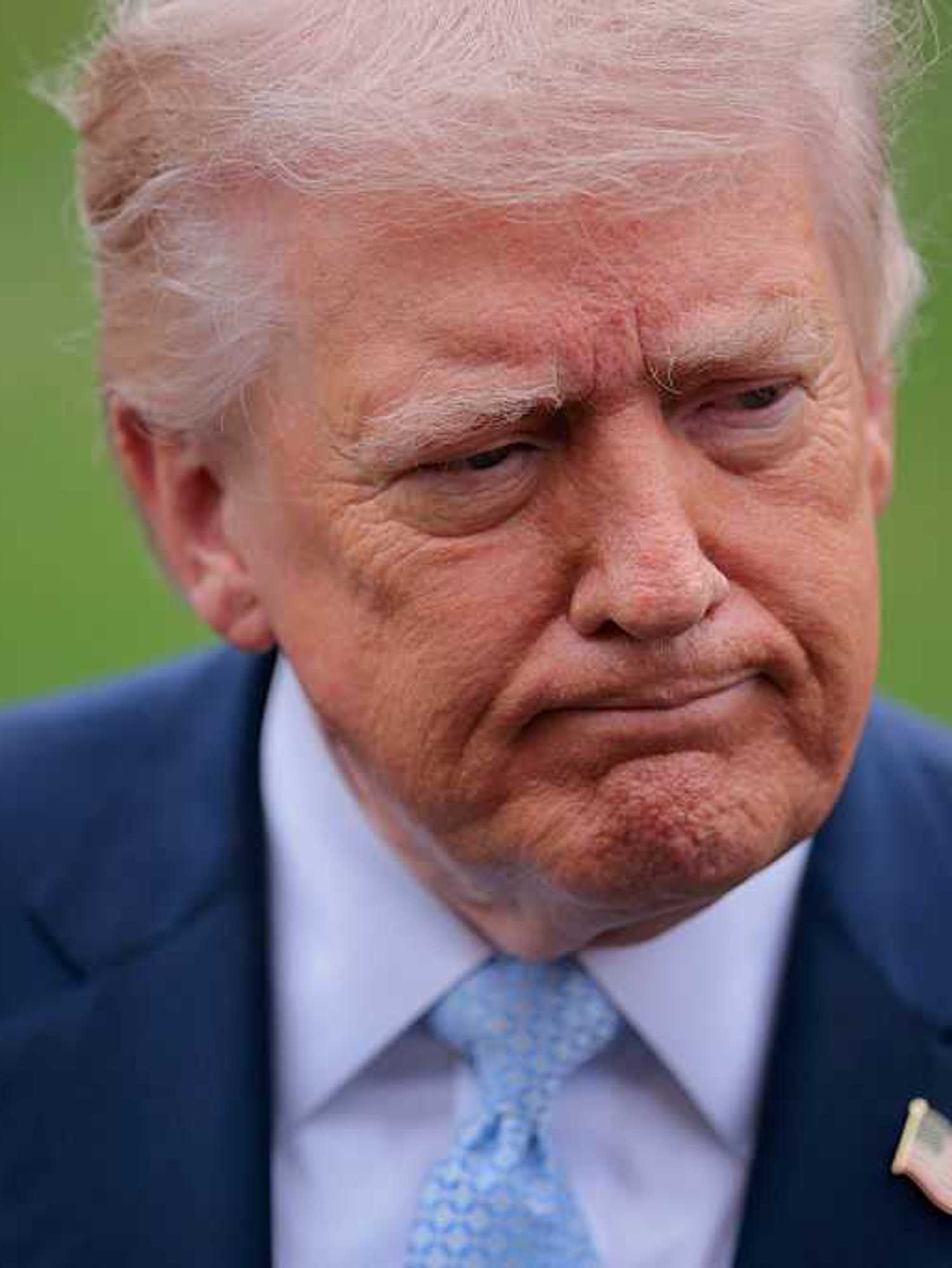 Donald Trump, a white man with short blonde hair and a blue suit, frowning slightly.