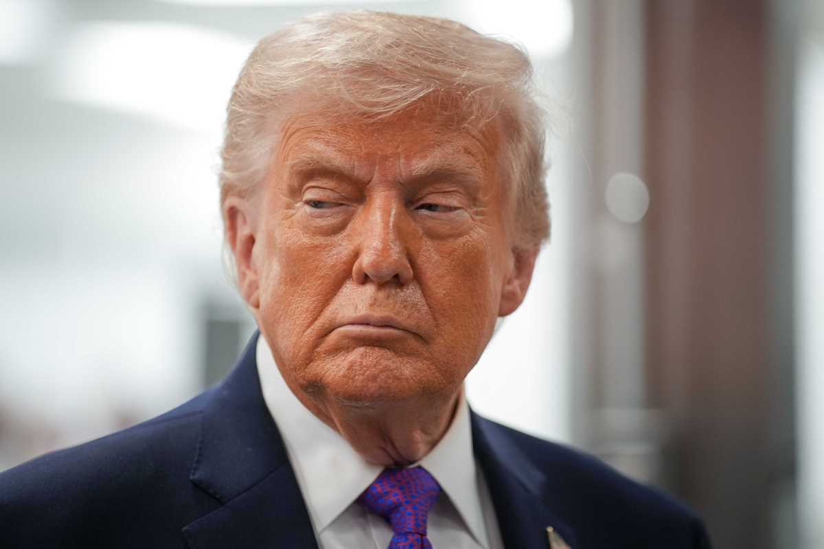 Donald Trump, a white man with short blonde hair, frowns as he looks at something to his right.