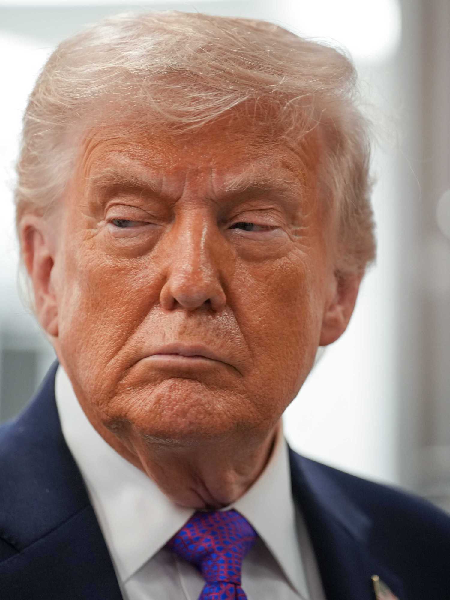 Donald Trump, a white man with short blonde hair, frowns as he looks at something to his right.