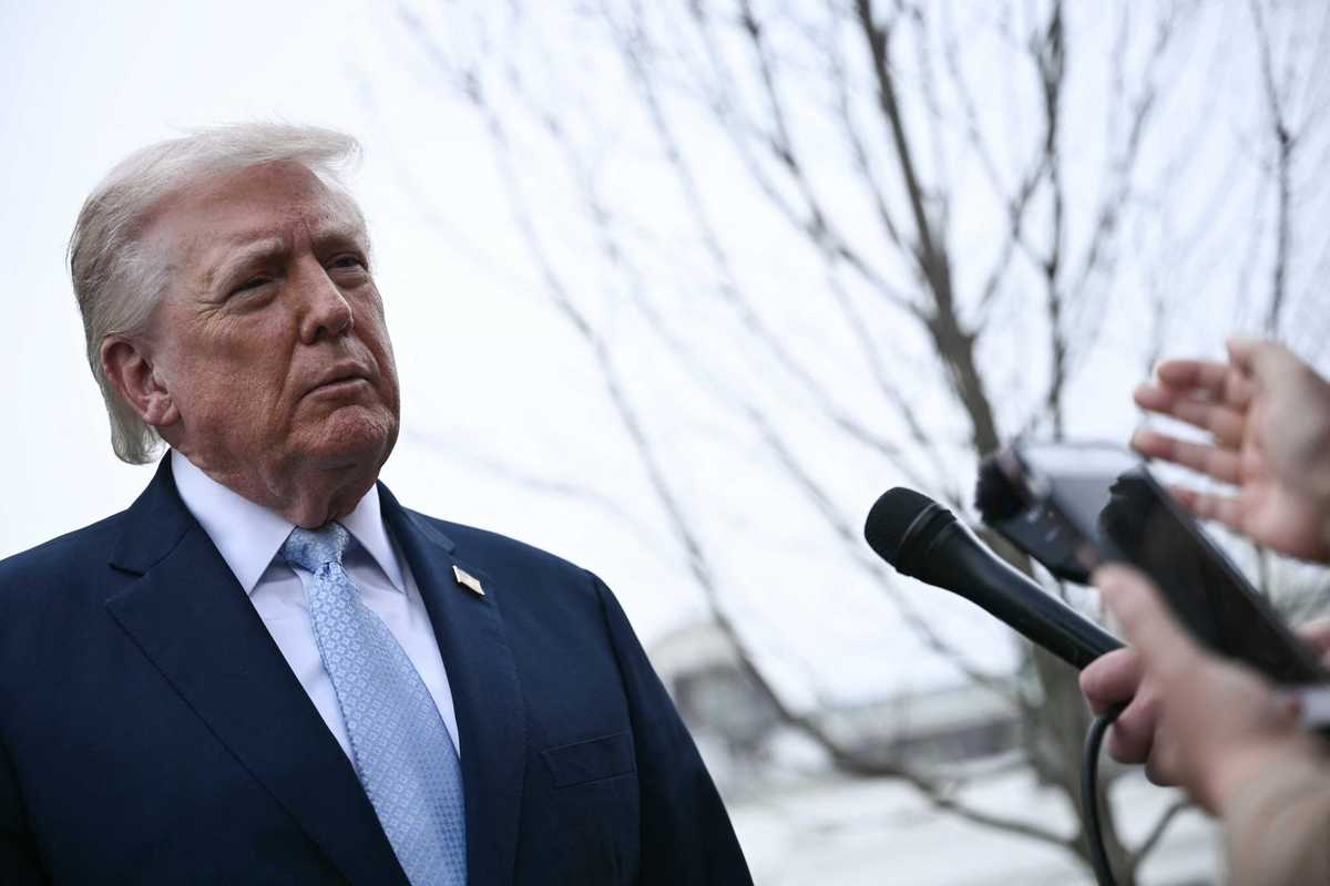 Donald Trump, a white man with short blonde hair in a black suit takes questions from reporters outside the White House.