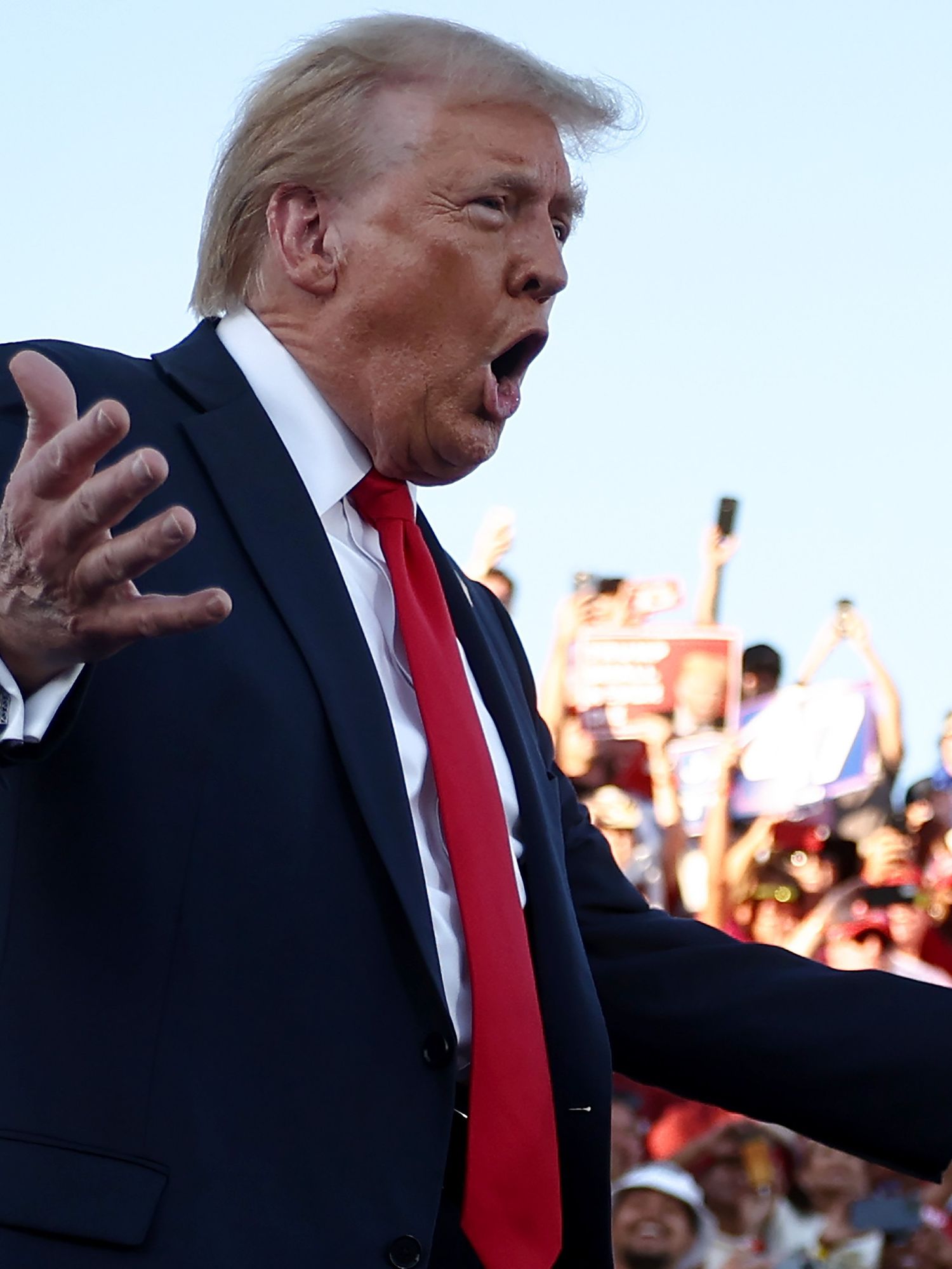 Donald Trump addresses supporters in Coachella, California, with his arms outstretched and mouth opened wide.